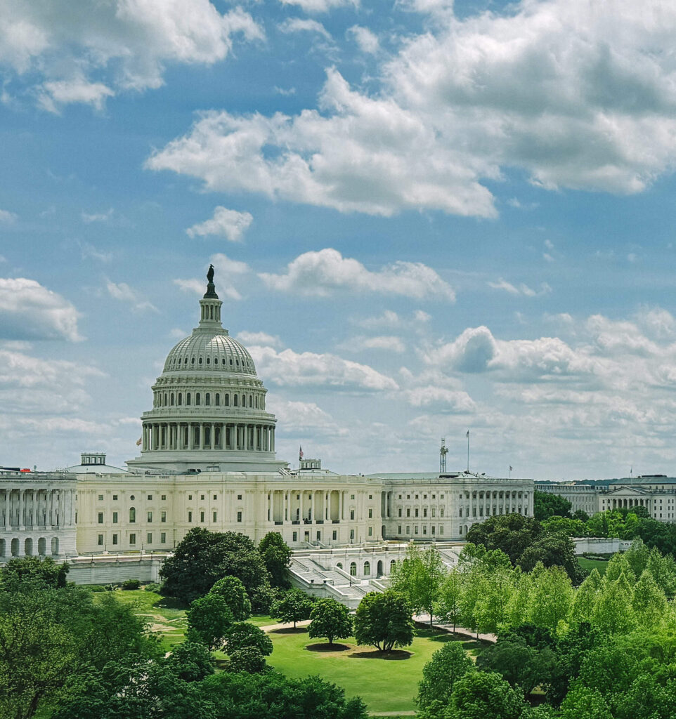 Ourdoor view of the capital building, green grass and a blue sky with lots of clouds.