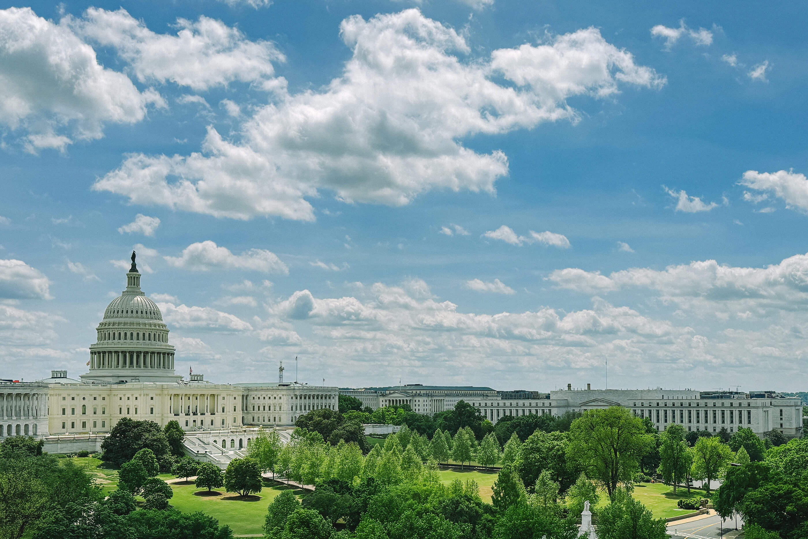 Ourdoor view of the capital building, green grass and a blue sky with lots of clouds.